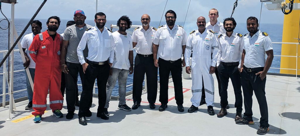 Crew members and officers standing together on the deck of a vessel at sea, posing for a group photo.