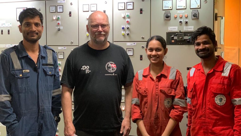Crew members in front of an electrical control panel onboard a vessel.