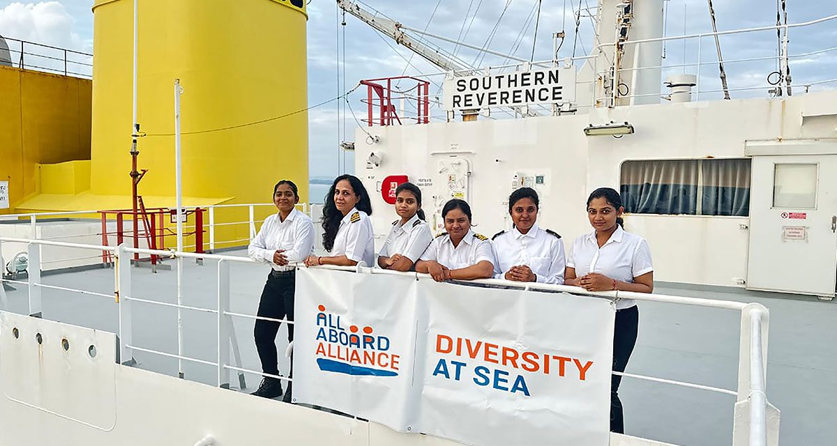 Six women seafarers in uniform standing on the deck of the Southern Reverence ship, next to a banner that reads &lsquo;Diversity at Sea&rsquo; and &lsquo;All Aboard Alliance.