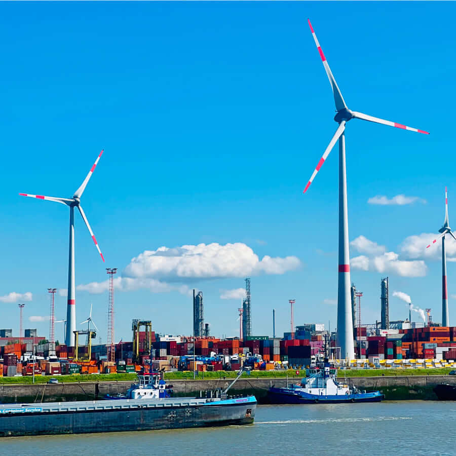 Wind turbines and cargo port with container ships under a clear blue sky