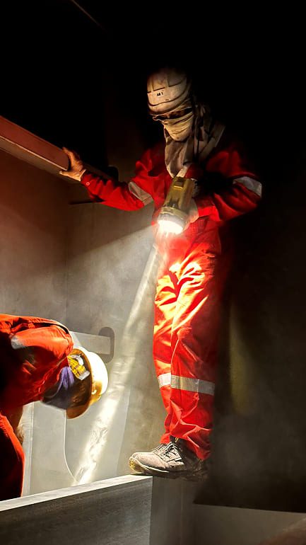 Captured inside a tank during the vessel's dry-dock period, this image uses light, scale and contrast to highlight the teamwork and mutual support required to carry out demanding shipboard tasks safely.