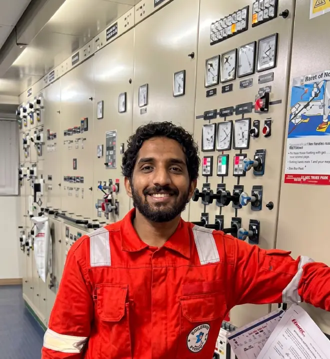 Smiling 4th Engineer Sidharth Dharmarajan in a red boiler suit standing inside the engine control room of the Stena Contender.