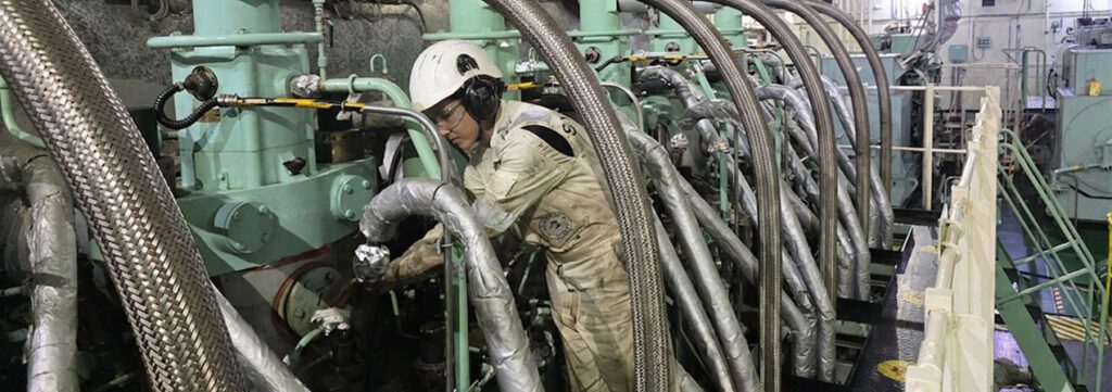Hifa Salim working on machinery inside the industrial engine room of a commercial cargo vessel.
