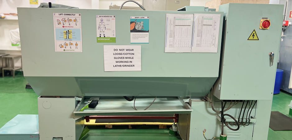 Industrial lathe machinery with safety warning signs inside the technical workshop of a marine vessel.