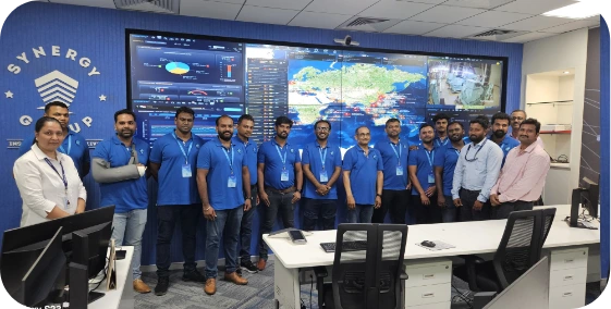 Technical team standing in the Synergy Remote Operations Optimisation Centre in front of a live fleet monitoring screen.